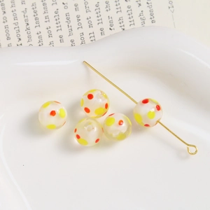 Detail shot of five 10mm dotted glass beads and a gold pin in a white heart dish
