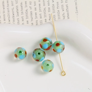 Macro view of 10mm light green glass beads with colorful polka dots on a metal pin