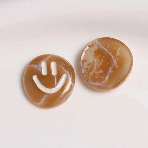 Detailed view of caramel marble resin charms with glitter and a minimal white smiley face