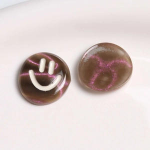Macro view of round resin charms with dark brown glitter and a white smiley face