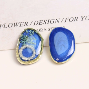Makro-Detail asymmetrischer Harzohrringe mit blauen Blumen, Perlen und goldenem Metallrand