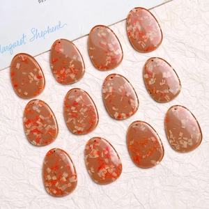 Macro view of 12 oval brown resin pendants with dried flower wood chip inserts for jewelry DIY