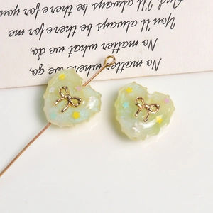 Detail of cream heart resin bead with glitter stars and gold bow for DIY jewelry making