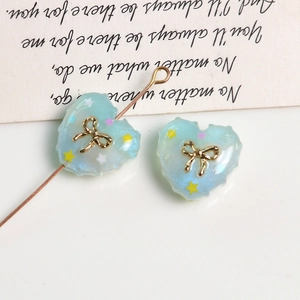 Macro detail of a glittery blue resin heart charm with a gold bow for DIY jewelry making