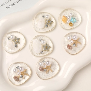 Detailed view of DIY resin ocean charms with seashells, pearls and stars on a white plate