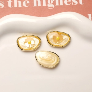 Detail of oval resin charms with yellow dried flowers and gold metal edges for DIY jewelry