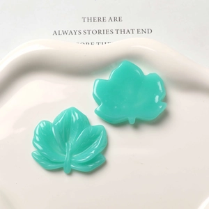 Detail of mint green resin maple leaf charms on a white ceramic dish for DIY jewelry