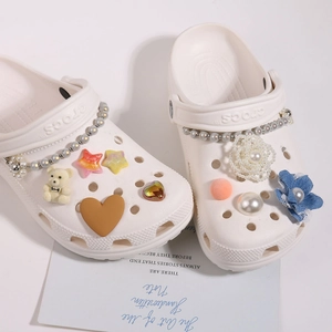 Detail von weißen Clogs mit Perlenkette, Blumen und 3D-Bären-Verzierungen