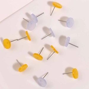 Detailed close-up of yellow and lavender acrylic flat round stud earrings on off-white surface