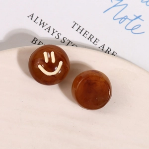 Detail view of brown marble resin stud earrings with white smiley face on ceramic plate