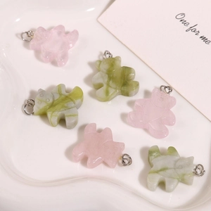Détail de breloques ours en quartz rose et jade avec anneaux argentés sur plateau blanc