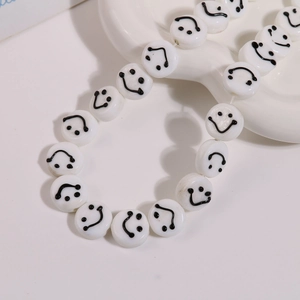 Macro shot of 14mm white round glass beads with black smiley face design on ceramic tray