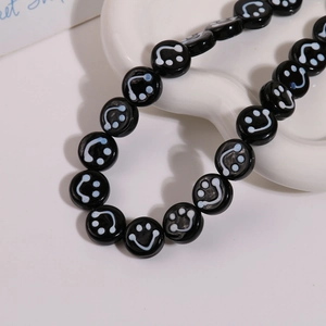 Detailed view of 14mm round glass beads featuring white smiley face patterns on black finish