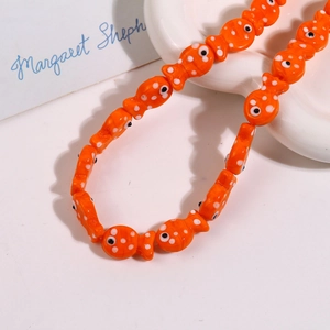 Macro view of orange ceramic fish bead with polka dots on a white textured tray