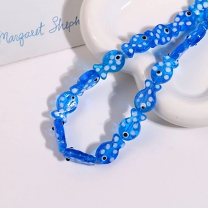 Close-up of handmade blue polka dot ceramic fish beads on a white heart ceramic tray