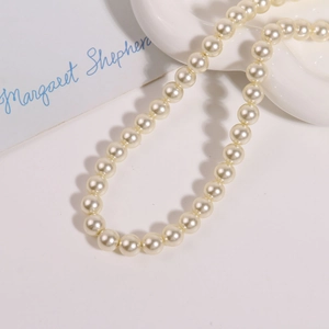 Gros plan de perles d'imitation blanc crème de 10mm sur un plateau en céramique blanche