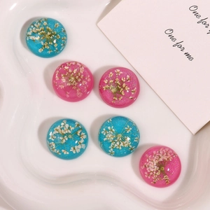Macro view of blue and pink resin cabochons with dried flowers and fine glitter