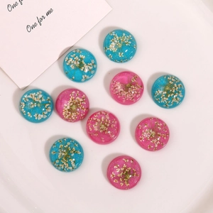 Flat lay of resin cabochons with embedded dried flowers and glitter in blue and pink