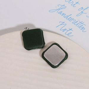 Detail of square dark green satin fabric buttons with smooth silver metal backing