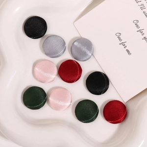Bottoni rotondi ricoperti di raso in vari colori presentati su un vassoio di ceramica