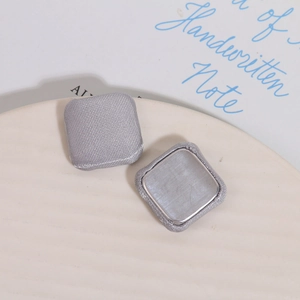 Macro detail of square silver fabric buttons with fine shimmering texture and gray base