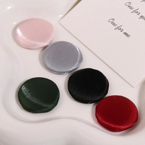 Vue détaillée de cinq boutons en tissu de soie colorés disposés sur une assiette blanche