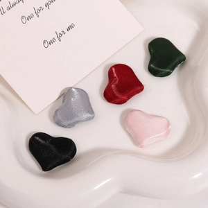 Macro detail of satin heart fabric charms in various colors on a ceramic tray