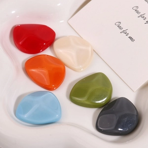 Close-up of colorful irregular resin charms in red, beige, and blue on a tray