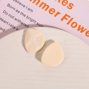 Macro shot of beige irregular resin stud earrings on a decorative white textured plate