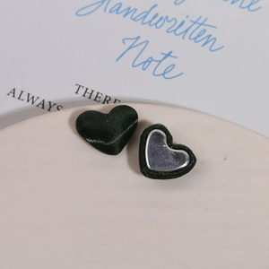 Macro view of dark green heart fabric buttons with silver metal base on a ceramic plate