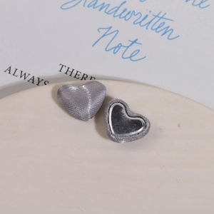 Close-up of heart-shaped DIY fabric buttons with silver silk and mirror finish on a ceramic tray