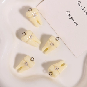 Dettaglio di 5 ciondoli a forma di denti in resina con apparecchio in vassoio bianco