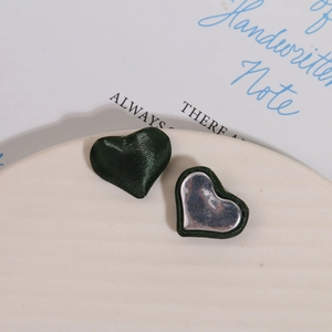 Close-up of heart-shaped dark green satin fabric charms with silver metal backing