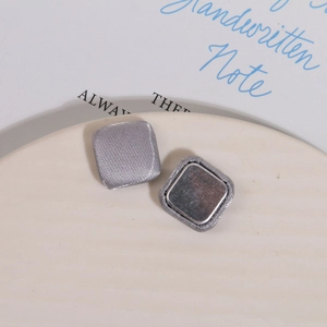 Close-up of grey fabric square magnetic buttons with twill texture on a ceramic tray