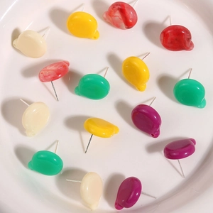 Macro shot of colorful pebble-shaped resin earring studs with metal pins in a white dish