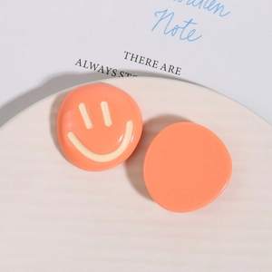 Detailed close-up of orange resin smile charms for DIY crafts on a cream tray