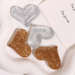 Macro detail of glitter-filled resin heart charms in gold and silver on ceramic tray