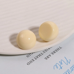 Detailed view of glossy cream Morandi resin ball studs on a white ceramic tray