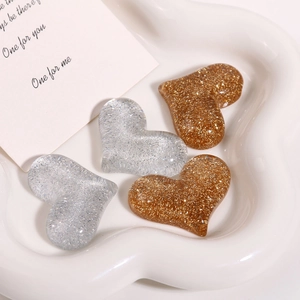 Detail of glitter-filled heart resin charms in gold and silver on a white tray