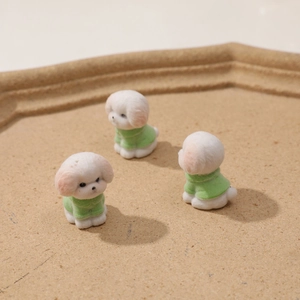 Dettaglio di tre figurine di cuccioli floccati bianchi con maglioni verdi per fai da te