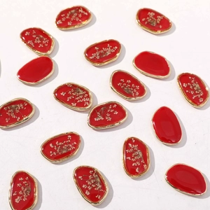 Dettaglio di ciondoli ovali in resina rossa con bordo dorato e fiori secchi per fai da te