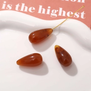 Close-up of three amber resin teardrop pendants on a white ceramic tray for DIY jewelry