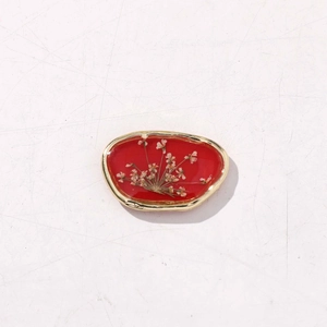 Dettaglio macro del ciondolo ovale in resina rossa con fiori secchi e bordo dorato