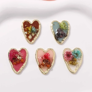 Vue macro de cinq pendentifs en résine en forme de cœur avec bord doré et fleurs séchées