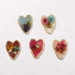 Vue à plat de cinq pendentifs en résine en forme de cœur avec fleurs séchées et or