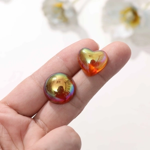 Iridescent heart and round resin cabochons for DIY crafts shown on a fingertip
