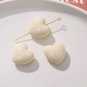 Vue macro de breloques cœur en résine crème pour bijoux DIY avec détail de tige dorée
