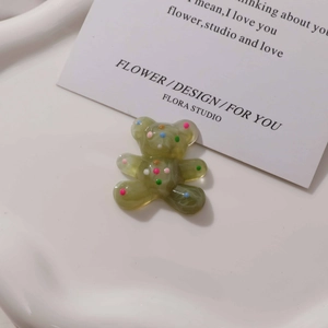 Macro view of transparent green resin bear charm with colorful dots on a white tray
