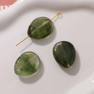 Macro view of olive green marble texture resin drop beads with gold metal pin for DIY jewelry