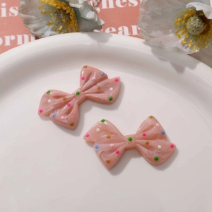 Detailed view of pink resin bow accessories with colorful polka dots on a white tray